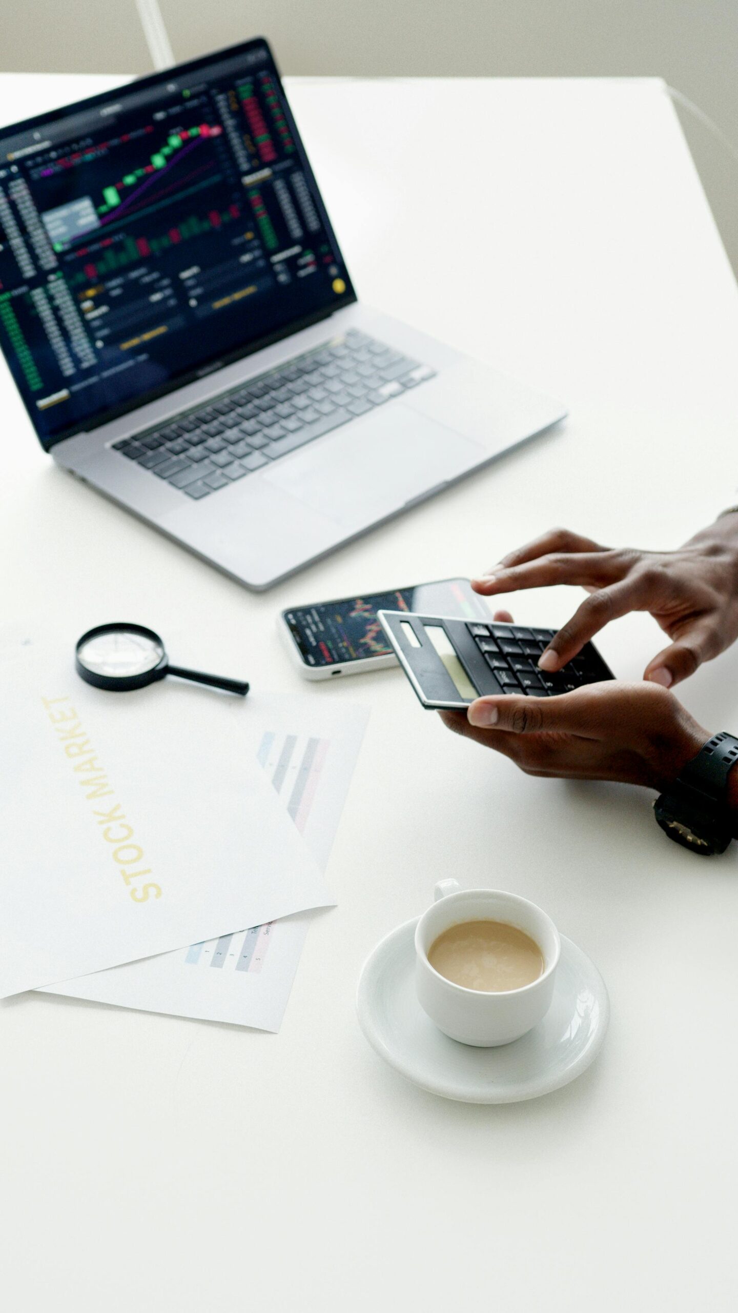 A businessman using a laptop and smartphone to analyze stock market trends indoors.